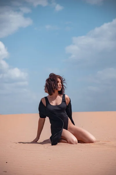 一个穿着黑色泳衣的女孩坐在沙漠的沙滩上 — 图库照片