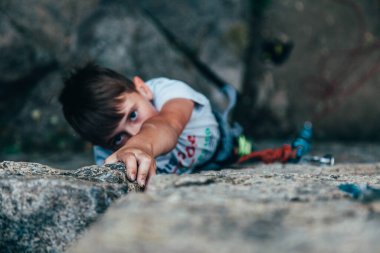 Beyaz tişörtlü genç ve güçlü bir kaya tırmanışçısı, kayaya tırmanıyor..