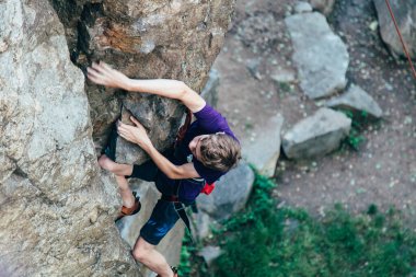Genç ve güçlü bir kaya tırmanışçısı, mor tişörtlü, uçuruma tırmanıyor..