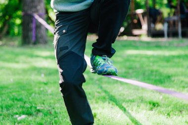 Genç adam ip üzerinde dengede duruyor ve zıplıyor. Yürüyen, zıplayan ve parkta ipte dengede duran bir adam..