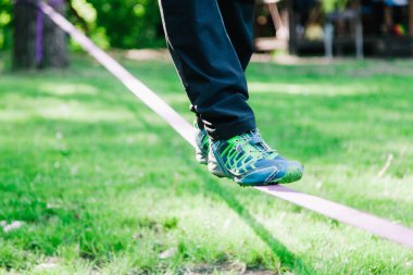 Genç adam ip üzerinde dengede duruyor ve zıplıyor. Yürüyen, zıplayan ve parkta ipte dengede duran bir adam..