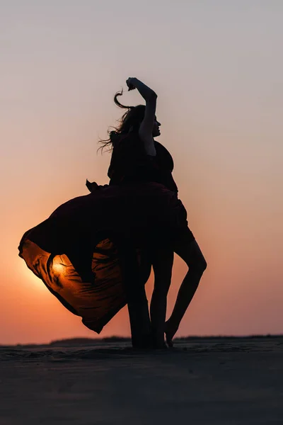Силуэт девушки в красном платье на закате в пустыне — стоковое фото