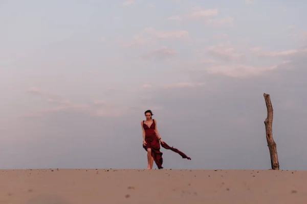 Σιλουέτα ενός κοριτσιού με κόκκινο φόρεμα το ηλιοβασίλεμα στην έρημο. — Φωτογραφία Αρχείου