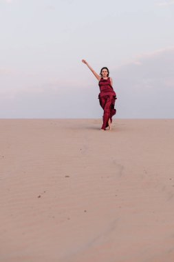 Çölde rüzgarda savrulan kırmızı elbiseli kız.