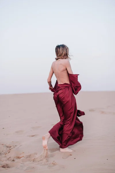Dívka s červenou látkou v paprscích zapadajícího slunce v poušti — Stock fotografie