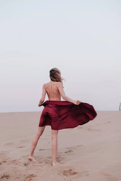 Fille avec un tissu rouge dans les rayons du coucher du soleil dans le désert — Photo