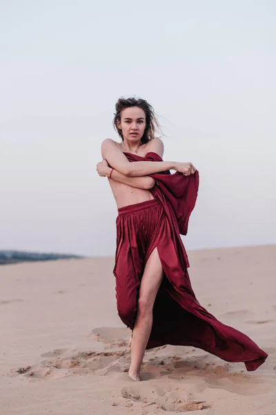 Fille avec un tissu rouge dans les rayons du coucher du soleil dans le désert — Photo