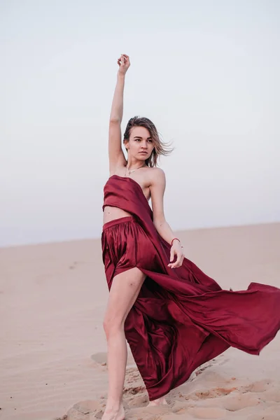 Chica con tela roja en los rayos del atardecer en el desierto — Foto de Stock