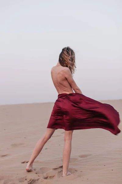 Fille avec un tissu rouge dans les rayons du coucher du soleil dans le désert — Photo