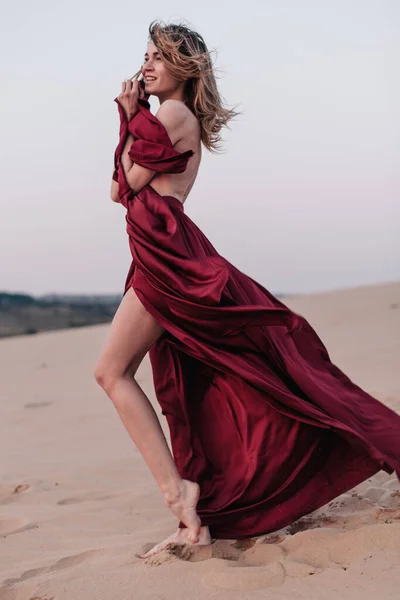 Dívka s červenou látkou v paprscích zapadajícího slunce v poušti — Stock fotografie