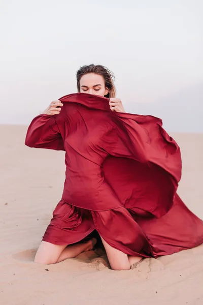 Девушка с красной тканью сидит на песке — стоковое фото