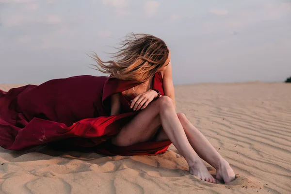붉은 드레스를 입은 소녀는 바람을 타고 사막에 앉아 있다 — 스톡 사진