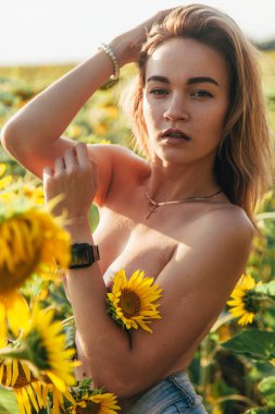 Genç üstsüz bir kız ayçiçeklerinde duruyor.