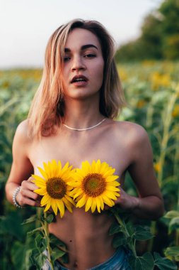 Genç üstsüz bir kız ayçiçeklerinde duruyor.