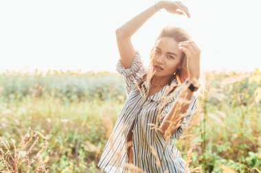 Tişörtlü genç bir kız ayçiçeklerinin içinde duruyor.