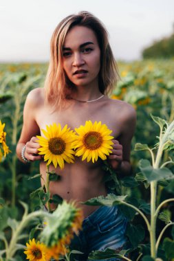 Genç üstsüz bir kız ayçiçeklerinde duruyor.