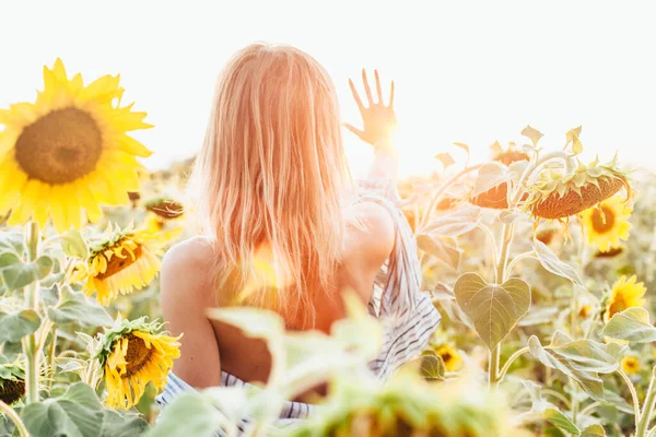 Tişörtlü genç bir kız ayçiçeklerinin içinde duruyor.