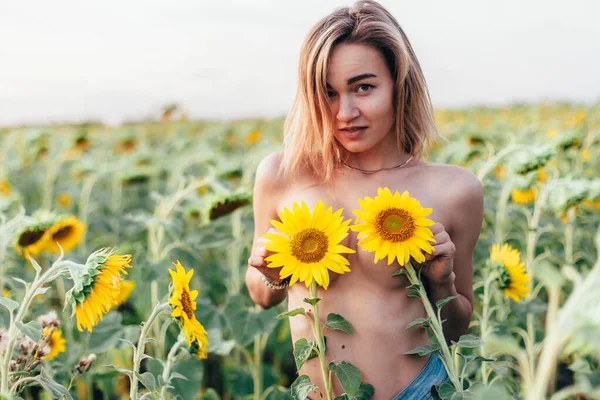Genç üstsüz bir kız ayçiçeklerinde duruyor.