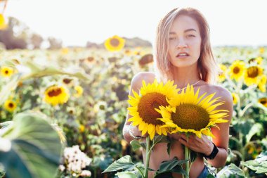 Genç üstsüz bir kız ayçiçeklerinde duruyor.