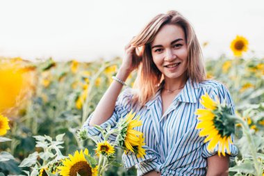 Tişörtlü genç bir kız ayçiçeklerinin içinde duruyor.