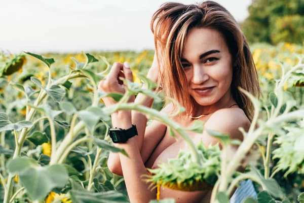 Genç üstsüz bir kız ayçiçeklerinde duruyor.