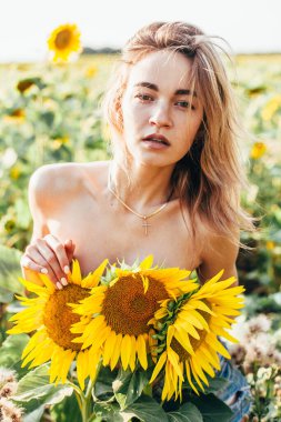 Genç üstsüz bir kız ayçiçeklerinde duruyor.