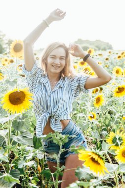Tişörtlü genç bir kız ayçiçeklerinin içinde duruyor.