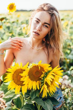 Genç üstsüz bir kız ayçiçeklerinde duruyor.