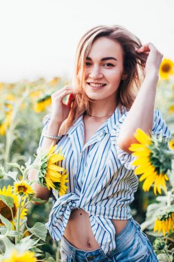Tişörtlü genç bir kız ayçiçeklerinin içinde duruyor.