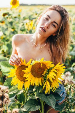 Genç üstsüz bir kız ayçiçeklerinde duruyor.