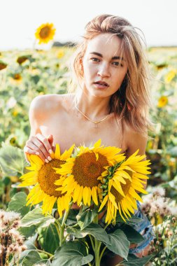 Genç üstsüz bir kız ayçiçeklerinde duruyor.