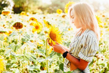Tişörtlü genç bir kız ayçiçeklerinin içinde duruyor.