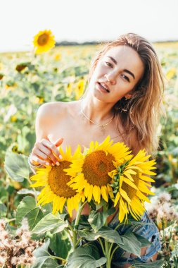 Genç üstsüz bir kız ayçiçeklerinde duruyor.