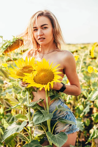 Genç üstsüz bir kız ayçiçeklerinde duruyor.