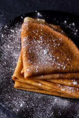 Koyu arka plan üzerine pudra şekeri ile krep yığını.