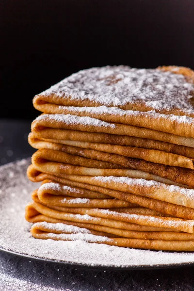 Stack of crepes with powdered sugar on dark background. Maslenitsa — Stock Photo, Image