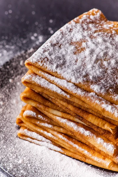 Stack of crepes with powdered sugar on dark background. Maslenitsa