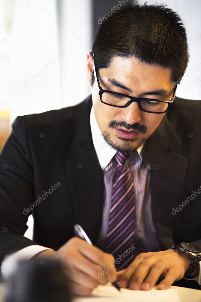 Portrait of young Japanese businessman working in the office. Handsome business man, in suit and shirt, working in the office. Close up.