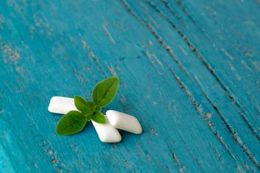 Açık mavi ahşap zemin üzerinde taze nane yaprağı olan bir grup nane şekerli sakız. Sakız parçaları. 