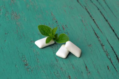 Açık yeşil ahşap zemin üzerinde taze nane yaprağı ve naneli sakız çiğneyen bir grup beyaz küp. Sakız parçaları. 