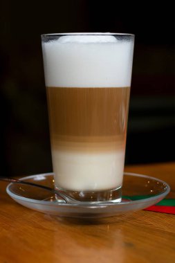 Uzun, şeffaf bardakta sıcak latte kahve siyah zemin üzerinde ahşap masa, düşük tuşlu yıldırımla dikey fotoğrafçılık..