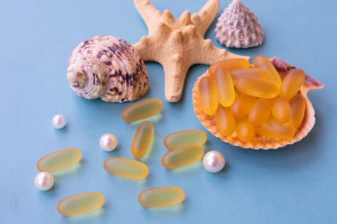 Omega 3 doğal balık yağının tıbbi kapsülleri mavi arka planda deniz kabuğunun yarısı üzerinde. Sağlıklı takviye kavramı