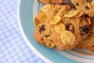 Masada mavi tabakta, üzerinde masa örtüsü olan bir grup mısır gevreği. Taze pişmiş yulaf bisküvileri..