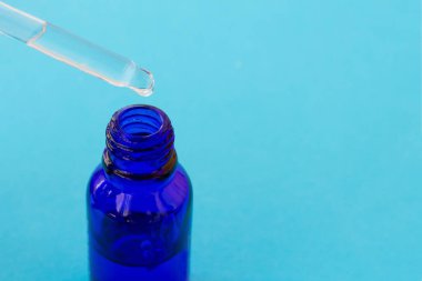 Şeffaf esansla ya da serumla doldurulmuş pipetli mavi cam şişe. Kozmetik yağ ve cam şişe damlacıklarıyla doldurulmuş Pipette. Boşluğu kopyala.