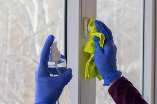 Hands are cleaning glass of window using wipe and spray bottle with antiseptic. Wet cleaning of home as concept of health care, self-hygiene and prevention of coronavirus spreading.
