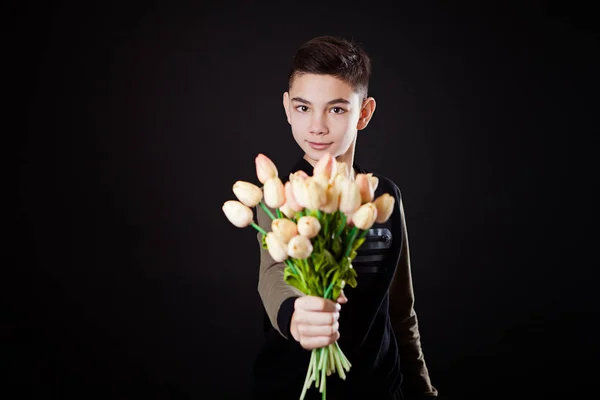 boy, a teenager in a black sweater gives, stretches forward a bouquet of flowers, tulips on a black background