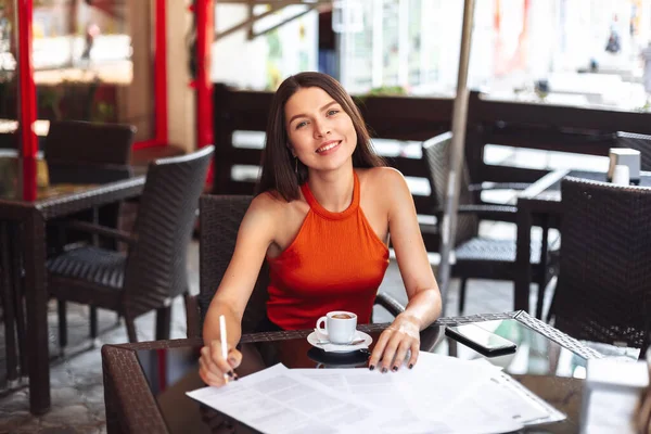 happy girl in a cafe over a cup of coffee signs documents. change of life, striving for success and future financial well-being, work in a convenient place.