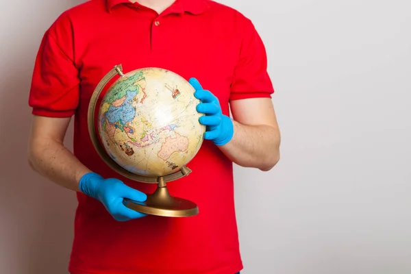 man in rubber medical gloves holds a globe in his hands