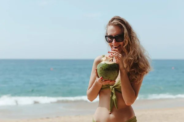 Flickan med kokosnöten på stranden. Flicka dricker kokosmjölk på stranden Stockbild