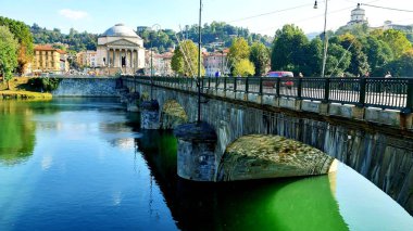 Torino, İtalya - 10 / 24 / 2019: Po nehrinin güzel manzarası, evlerin ve suyun üzerindeki köprünün inanılmaz yansıması. Açık mavi gökyüzü ve arka planda sonbahar renkli ağaçlar. 